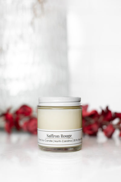 Saffron Rouge 4 oz candle by Willow Hill Soap Company with red flowers in background. 
